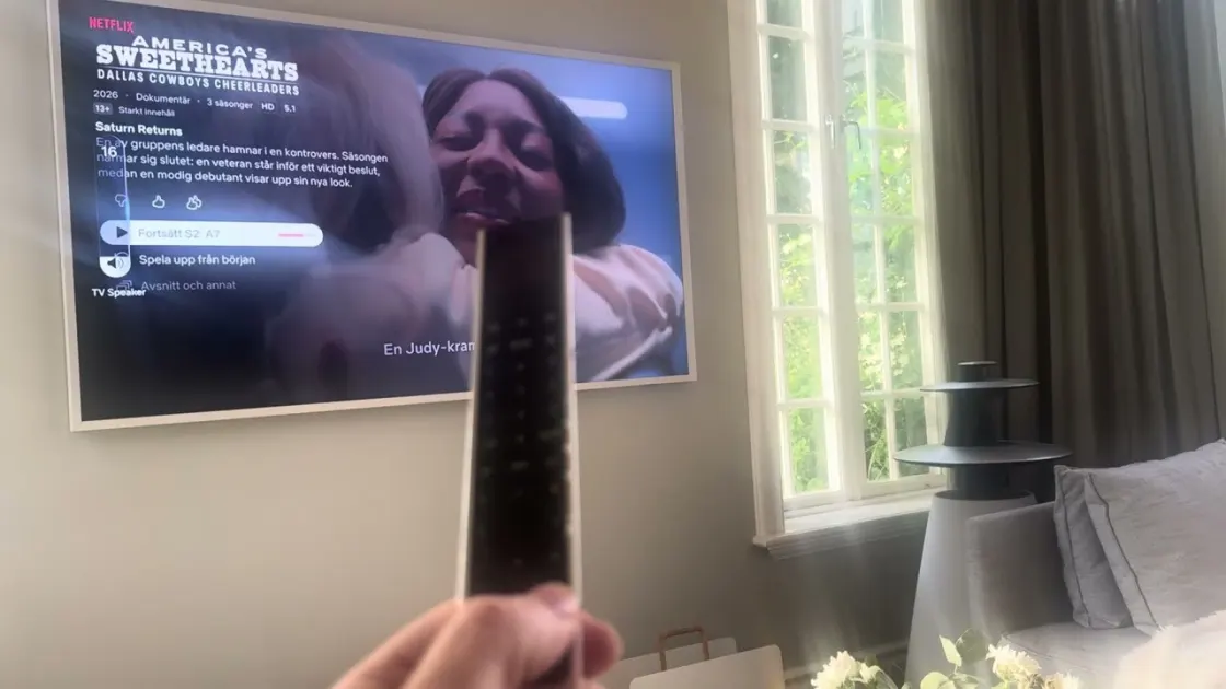 A Beoremote One held up in front of a Samsung The Frame showing Netflix
